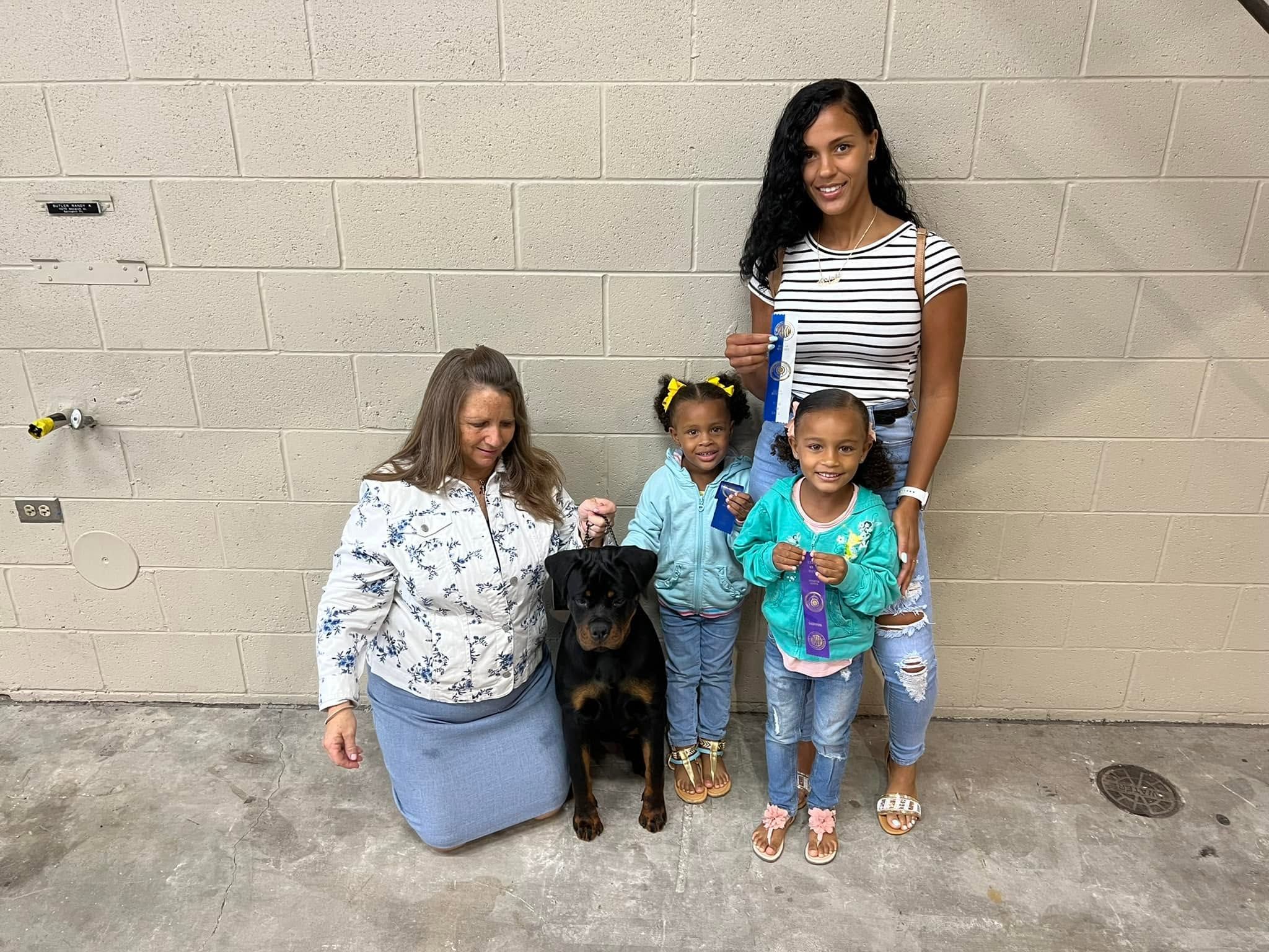 Truth on lead with her handler and family against a block wall, two young girls holding show ribbons
