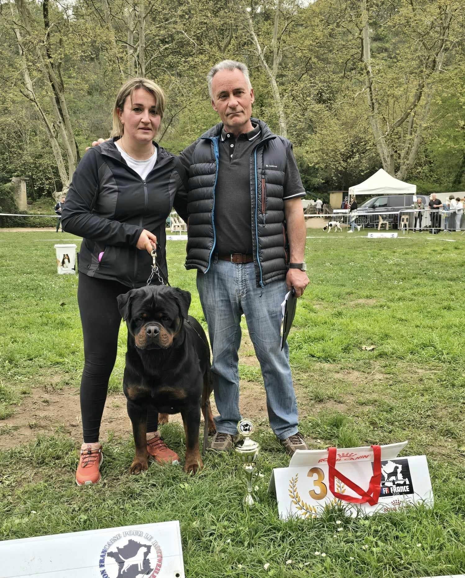 Uvo on lead with his handler and the judge at a French Rottweiler club show, a third-place trophy beside them